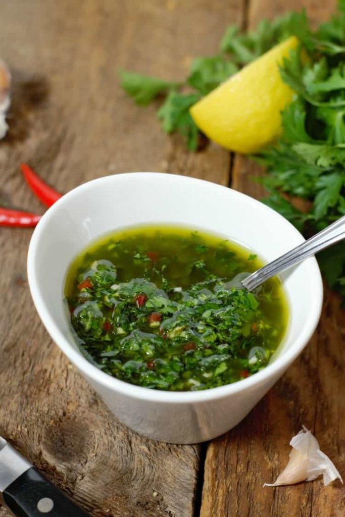 authentic chimichurri served in a white dish surrounded by various ingredients