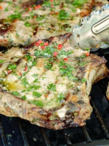grilled pork chops topped with chimichurri on a bbq grill