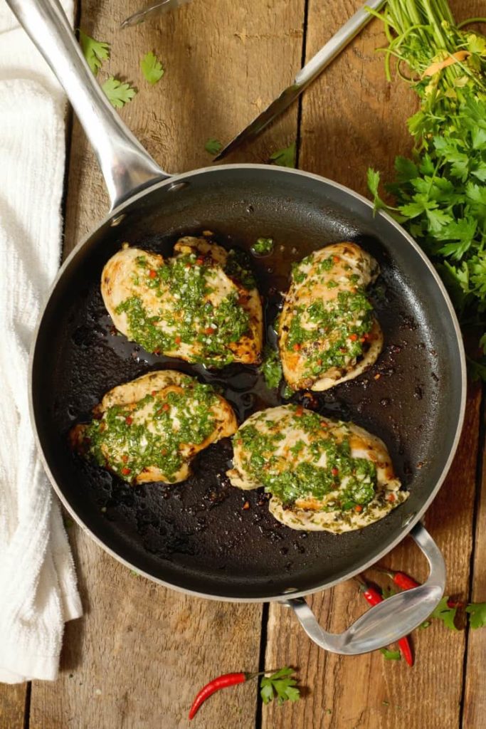 overhead shot of freshly four pan seared chicken breasts in a pan topped with chimichurri sauce
