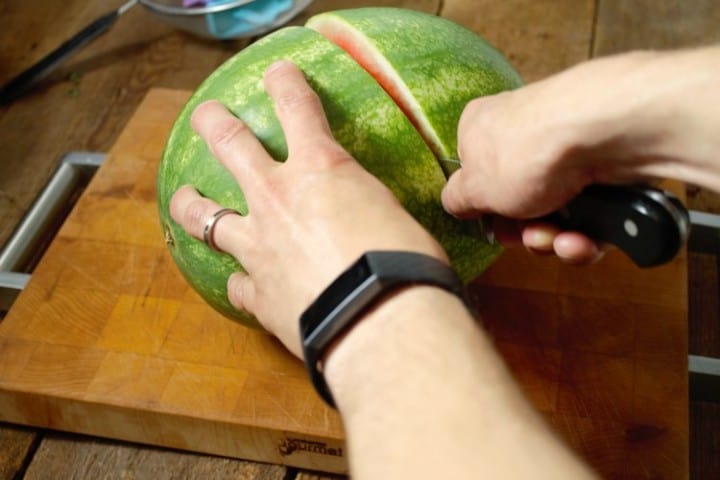 a watermelon being cut in half on a wooden cutting board
