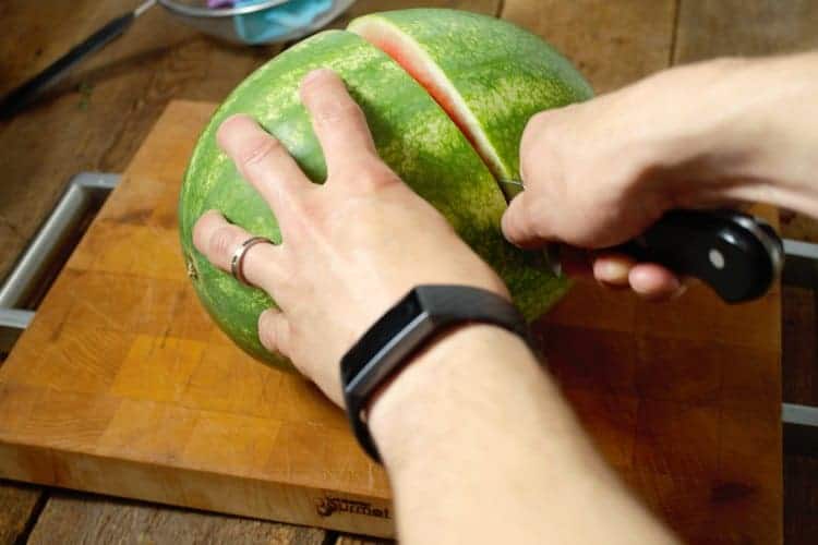 a watermelon being cut in half on a wooden cutting board