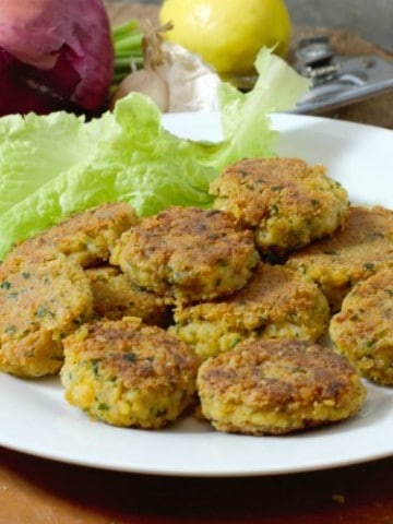 homemade falafel patties on a white plate surrounded by garnishes