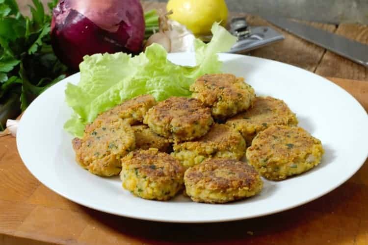 homemade falafel patties on a white plate surrounded by garnishes