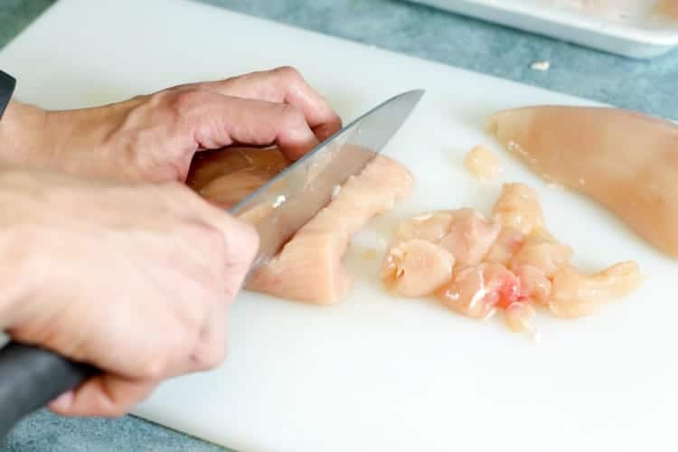 dicing raw chicken on a cutting board