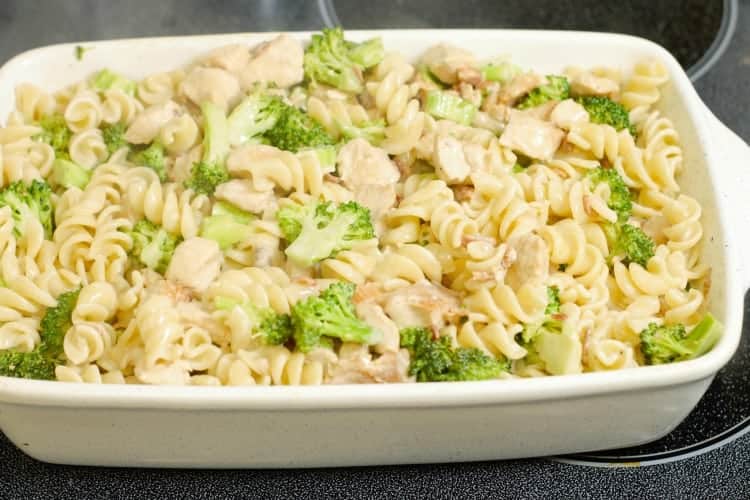 chicken, broccoli, bacon, pasta, and coconut milk being mixed in a casserole dish