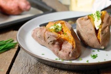 whole baked sweet potatoes garnished with butter and chives on a rustic plate