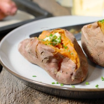 whole baked sweet potatoes garnished with butter and chives on a rustic plate