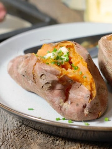 whole baked sweet potatoes garnished with butter and chives on a rustic plate