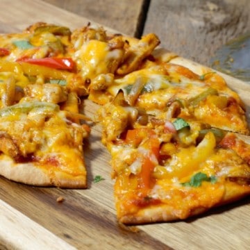 close up of a sliced chicken fajita naan pizza on a wooden serving board