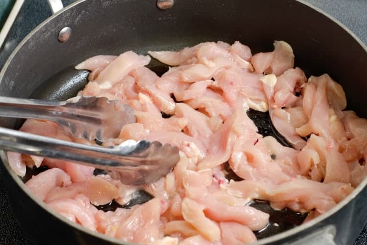 cooking raw chicken breast strips in a pan
