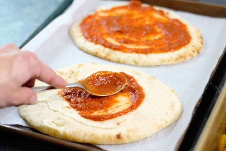 spreading tomato sauce on a naan bread