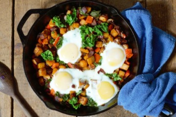 sweet potato hash with bacon, onion, bell pepper, kale, and eggs served in cast iron pan