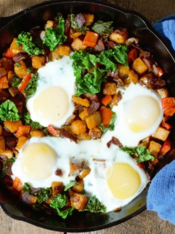 sweet potato hash with bacon, onion, bell pepper, kale, and eggs served in cast iron pan