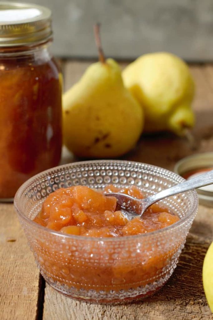 vertical image of pear preserves served in a small glass dish on a harvest table