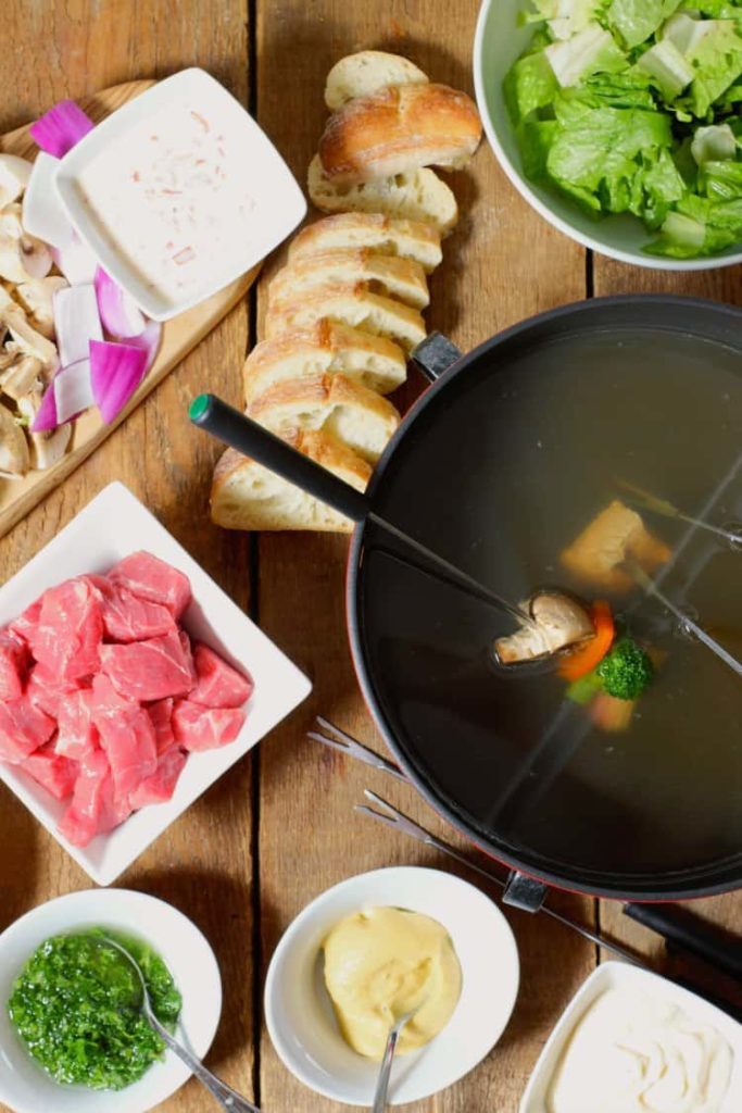 overhead shot of beef fondue served on a wooden table with various condiments and garnishes