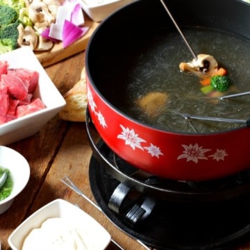 various food items being cooked in broth in a fondue pot