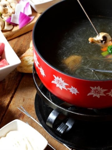 various food items being cooked in broth in a fondue pot