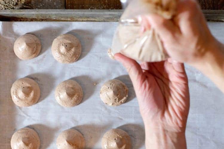 piping chocolate meringue cookies onto a parchment lined baking sheet