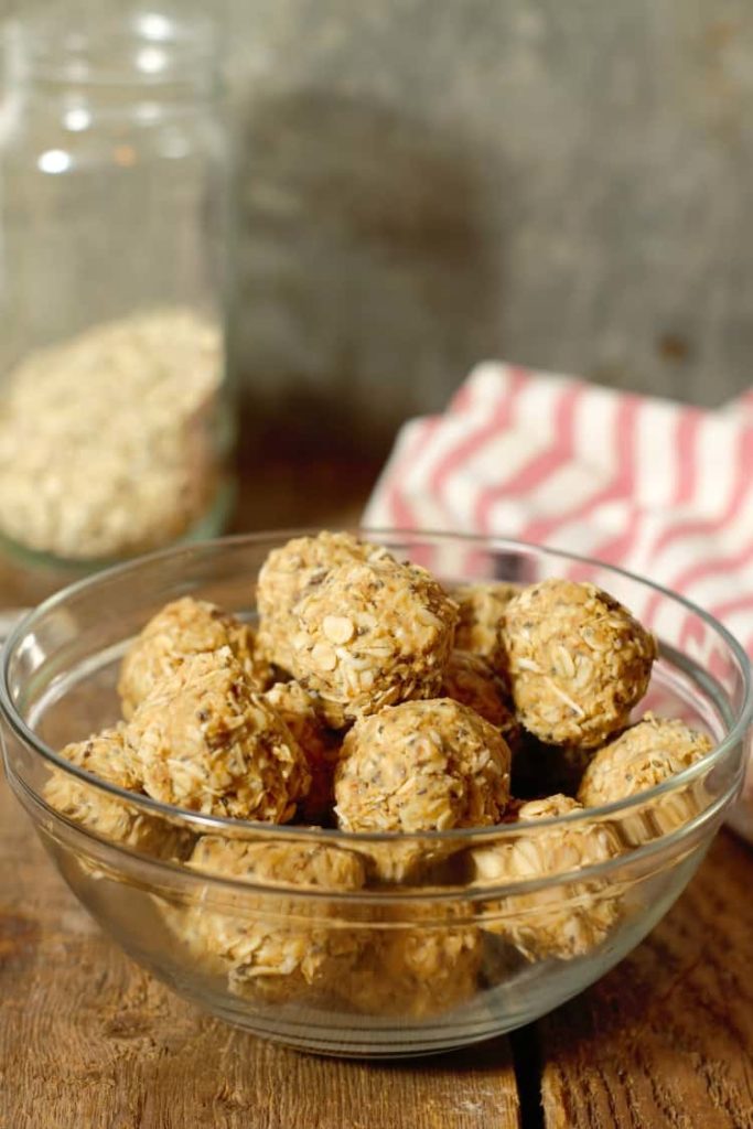 vertical image of peanut butter protein balls in a glass bowl on a wood board tabletop