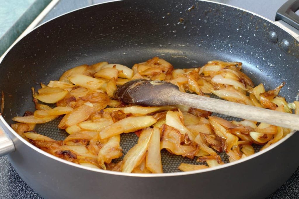 caramelized onions in a non stick pan being stirred with a wooden spoon
