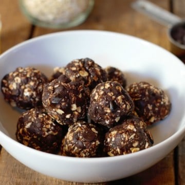 dark chocolate date balls in a white bowl on a wooden tabletop