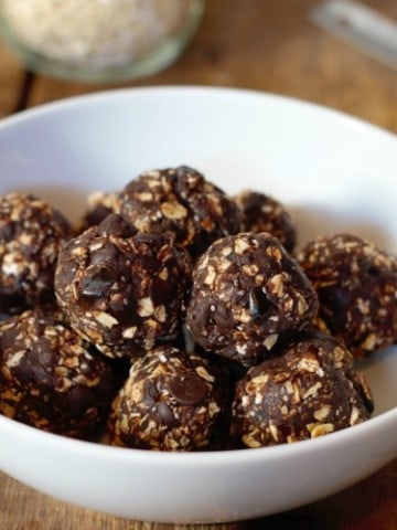 dark chocolate date balls in a white bowl on a wooden tabletop