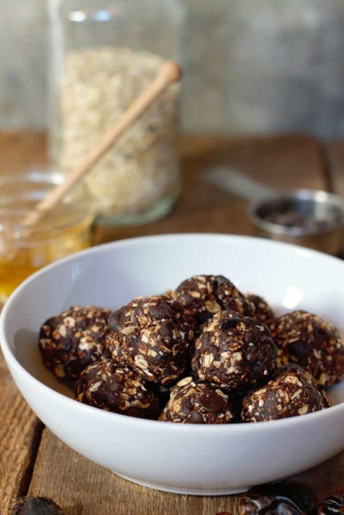 vertical picture of dark chocolate and date energy balls in a white porcelain bowl