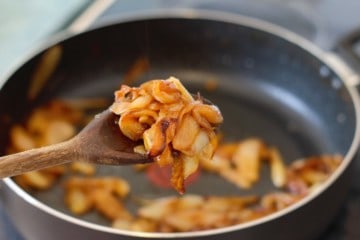 caramelized onions being picked up with a wooden spoon over a pan