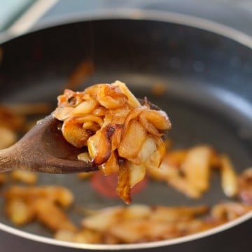 caramelized onions being picked up with a wooden spoon over a pan