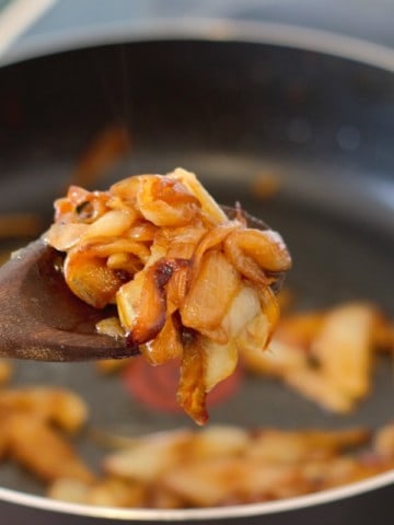 caramelized onions being picked up with a wooden spoon over a pan