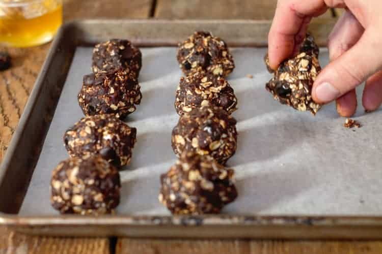 chocolate date balls being formed by hand an placed on a sheet tray