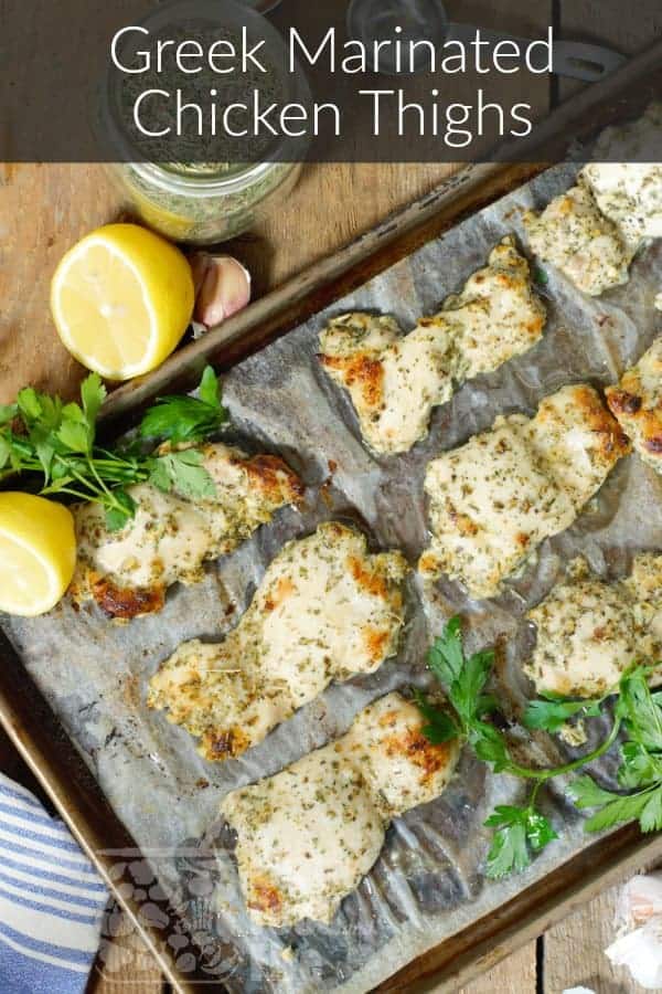 overhead shot of fully baked greek marinated chicken thighs on a grey sheet tray surrounded by various ingredients