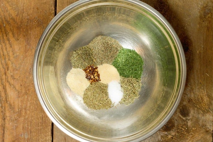 various herbs and spices used to make italian seasoning in a stainless steel bowl