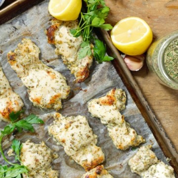 overhead shot of greek marinated chicken thighs on a sheet pan surrounded by various seasonings