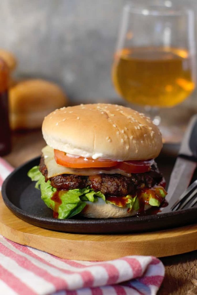 vertical image of a fully loaded moose meat burger on a cast iron serving platter