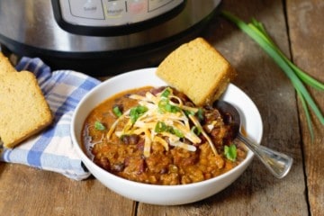 instant pot chili served in a white bowl and topped with shredded cheese and green onions