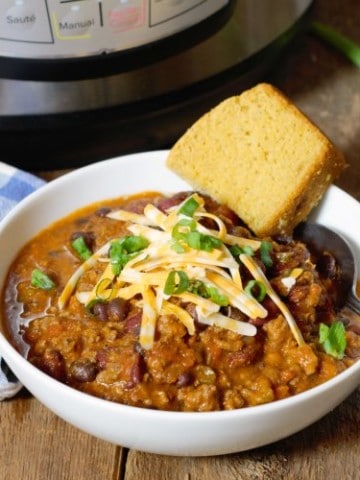 instant pot chili served in a white bowl and topped with shredded cheese and green onions