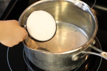 measuring out ½ cup of sugar in a pot