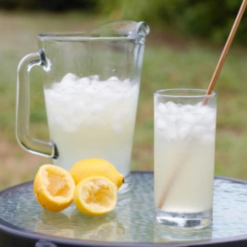 old fashioned lemonade served in a glass with a metal straw on a table outside