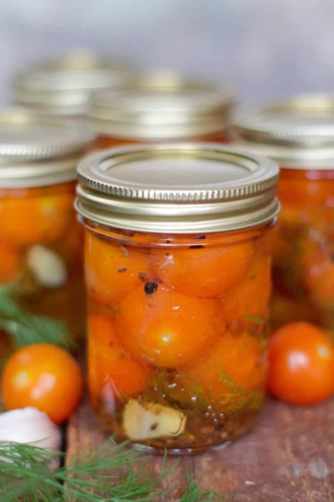 pickled cherry tomatoes in mason jars on a wood board surface