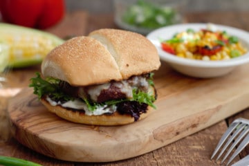 grilled tex-mex cheeseburger on a wooden serving board with grilled corn and peppers in the background