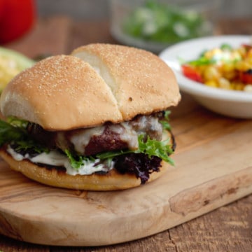 grilled tex-mex cheeseburger on a wooden serving board with grilled corn and peppers in the background