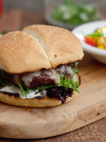 grilled tex-mex cheeseburger on a wooden serving board with grilled corn and peppers in the background