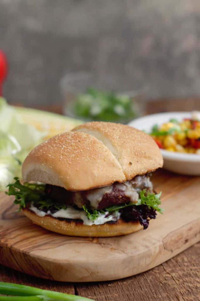 tex-mex cheeseburger served on a wooden board with veggies in the background