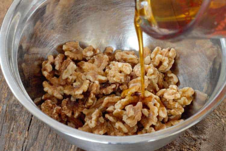 pouring maple syrup over raw walnuts in a steel bowl