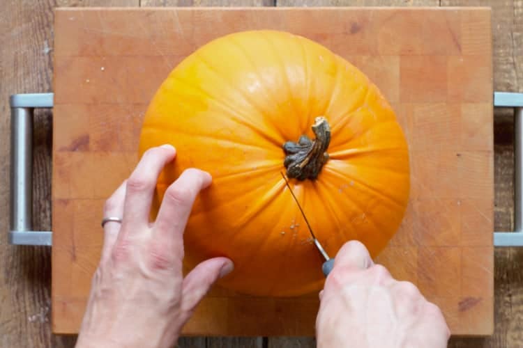 cutting a pumpkin in half with a large knife