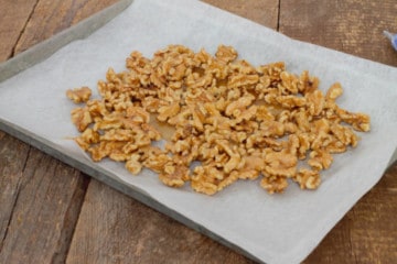 raw walnuts coated with maple syrup spread out on a parchment lined sheetpan