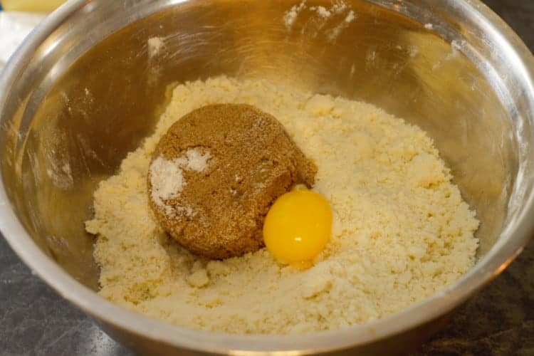 brown sugar and egg yolk being added to the flour and butter mixture