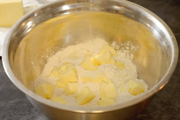 adding cubed butter to a mixing bowl with flour