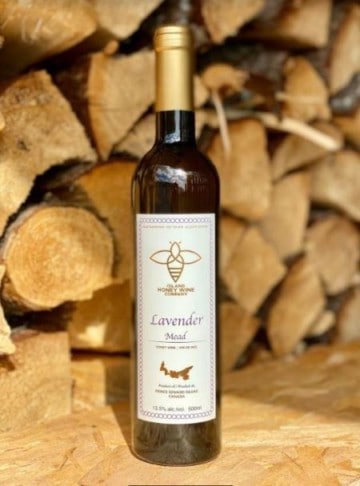 a bottle of lavander mead in front of a stack of dried firewood